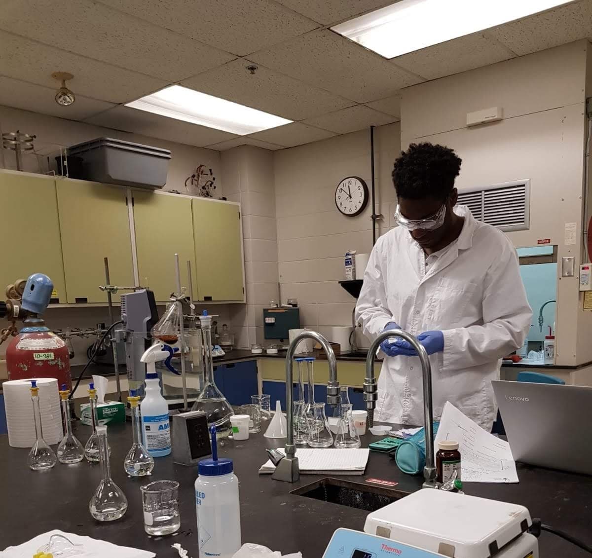 Un homme noir en blouse blanche travaille avec du matériel dans un laboratoire de chimie.